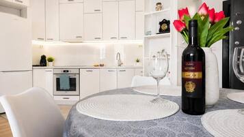 Une cuisine moderne avec des meubles blancs, une table à manger avec des sets de table, une bouteille de vin et un vase rempli de fleurs rouges.
