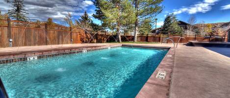 Una piscina rectangular con agua azul cristalina, rodeada por una valla de madera y árboles.
