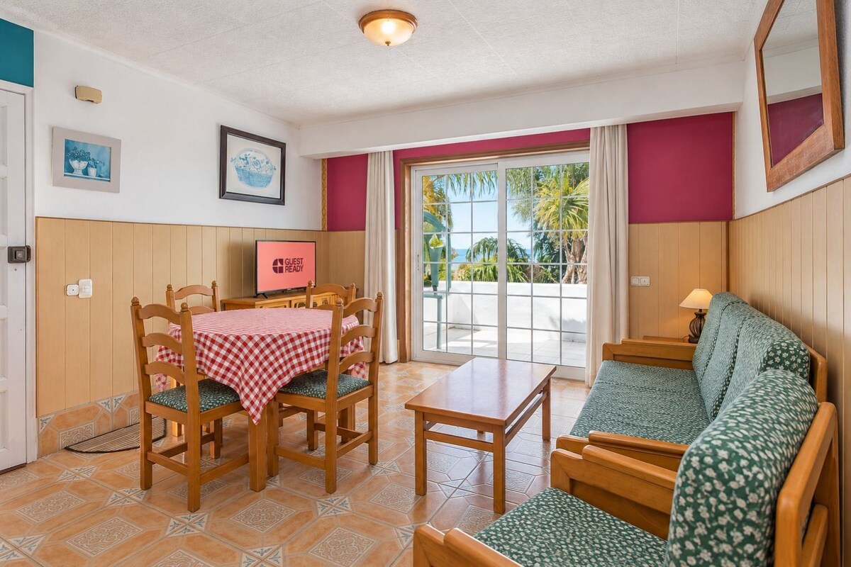 A room with a dining table, chairs, a sofa, a television, and a view of the outdoors.