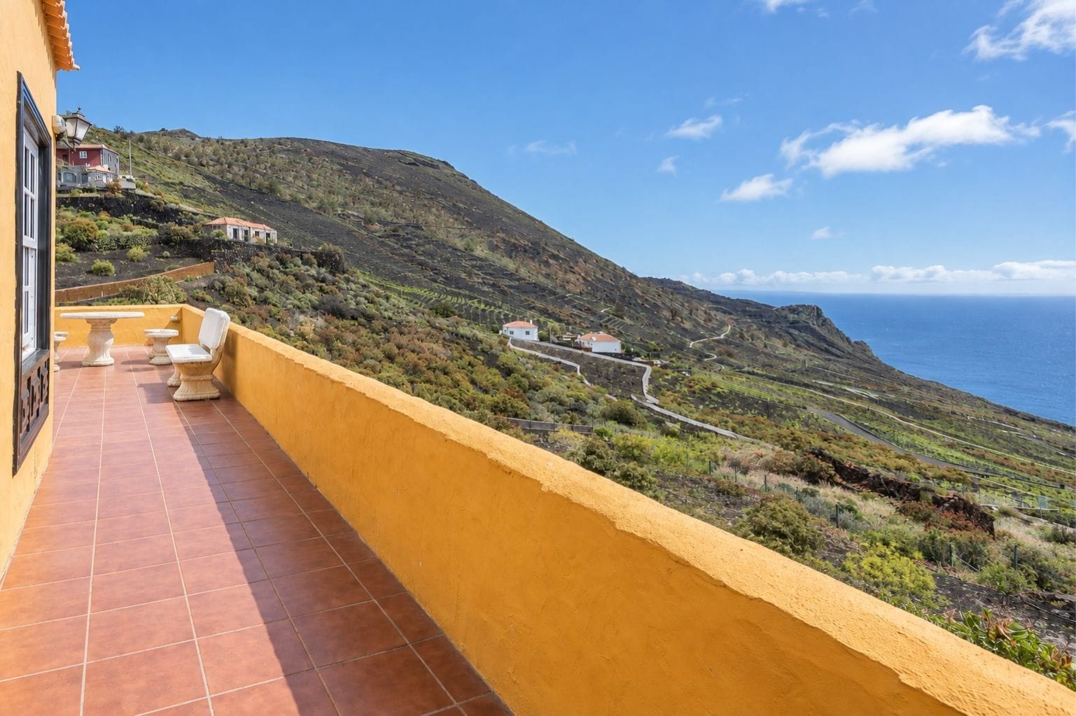 A balcony with a view of a coastal landscape, including terraced fields and a winding road.