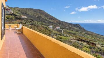 A balcony with a view of a coastal landscape, including terraced fields and a winding road.