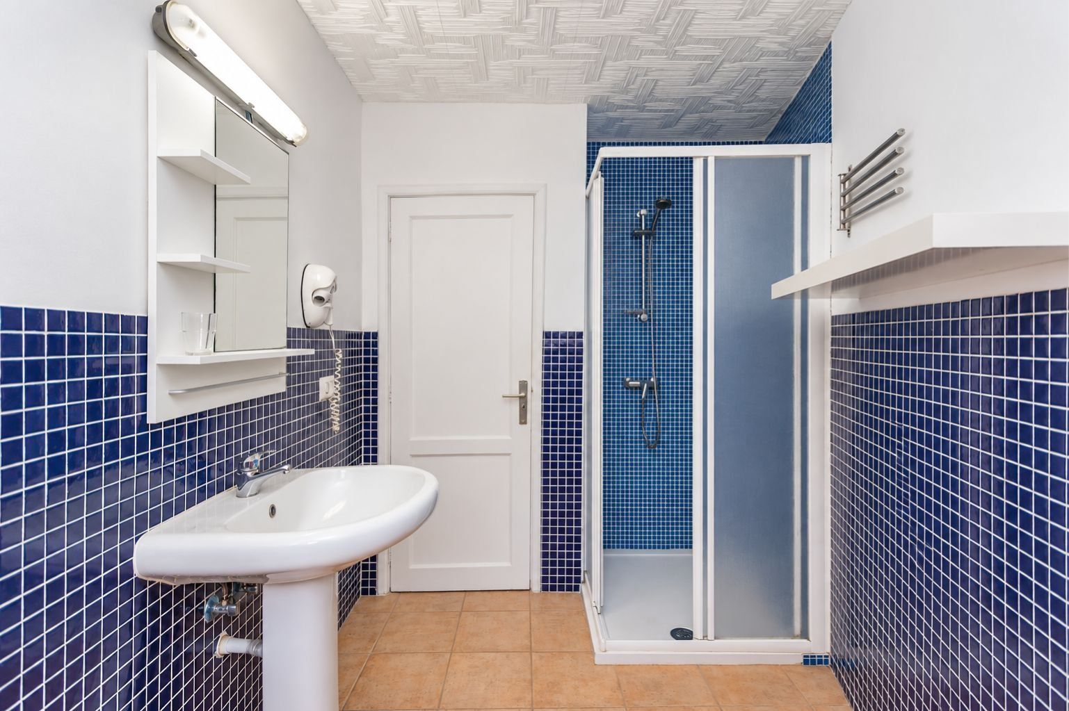 Un baño con lavamanos blanco, un espejo, cabina de ducha y paredes con azulejos azules.