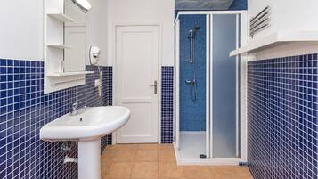 Un baño con lavamanos blanco, un espejo, cabina de ducha y paredes con azulejos azules.