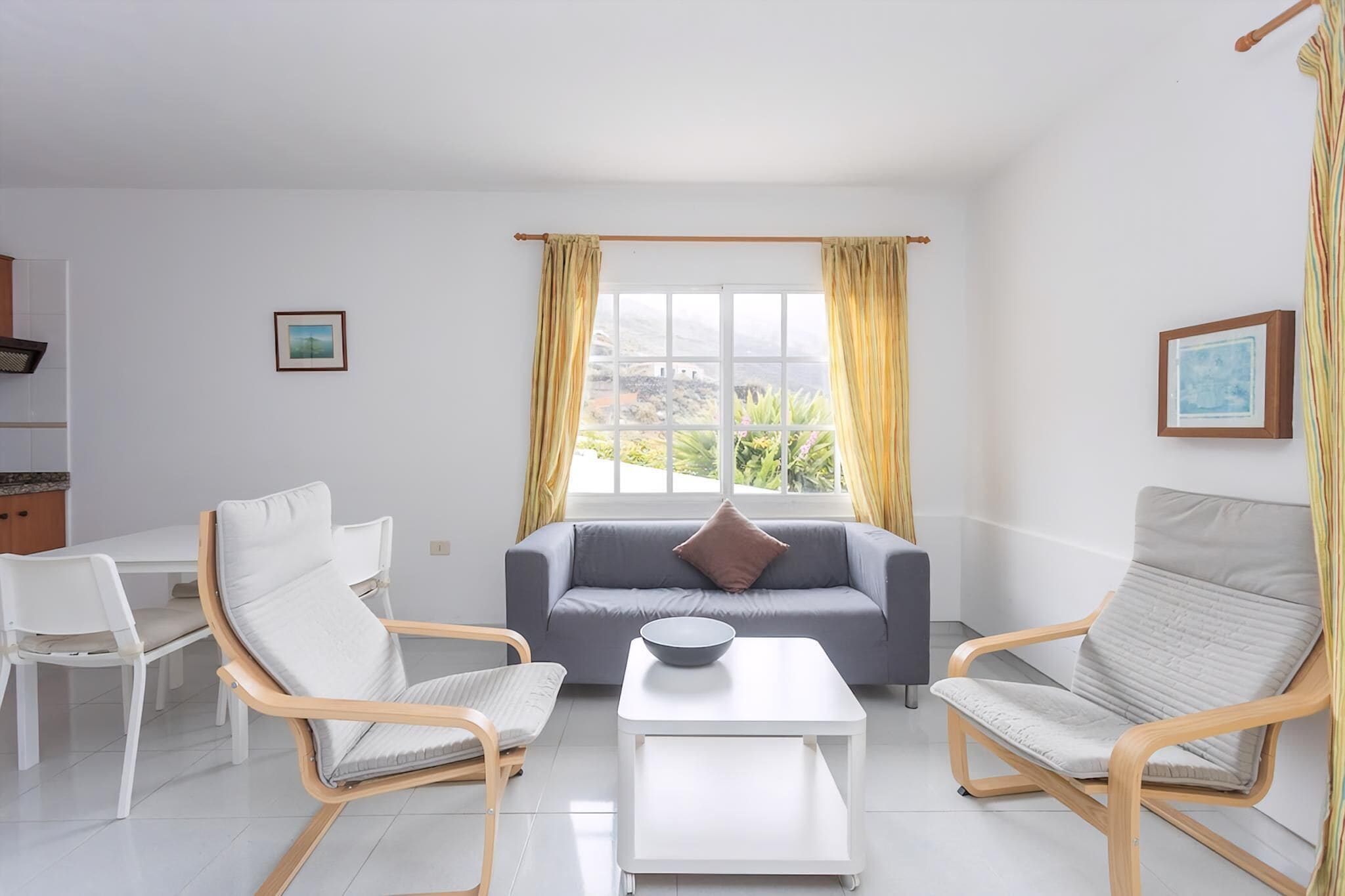 Una sala de estar con sofá, dos sillones, una mesa de centro y una ventana con cortinas.