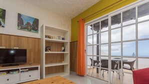 A living room with a TV, wooden shelves, a table, and a large window with a view. - Guestready - Colon Eva (Fuencaliente de la Palma)