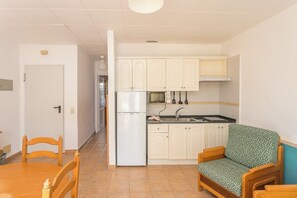 A compact kitchen with white cabinets, a refrigerator, a microwave, and a sink. There is a wooden dining table with chairs and a patterned armchair. - Guestready - Colon Eva (Fuencaliente de la Palma)