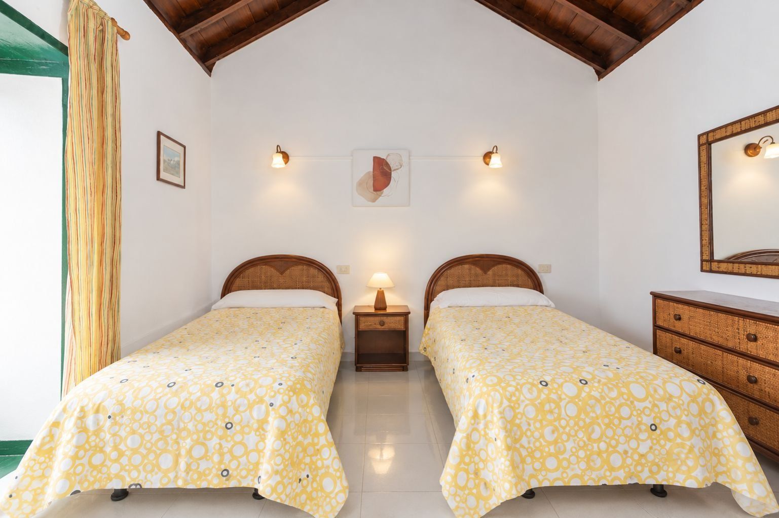 A room with two beds, a wooden dresser, a mirror, and wall-mounted lights.