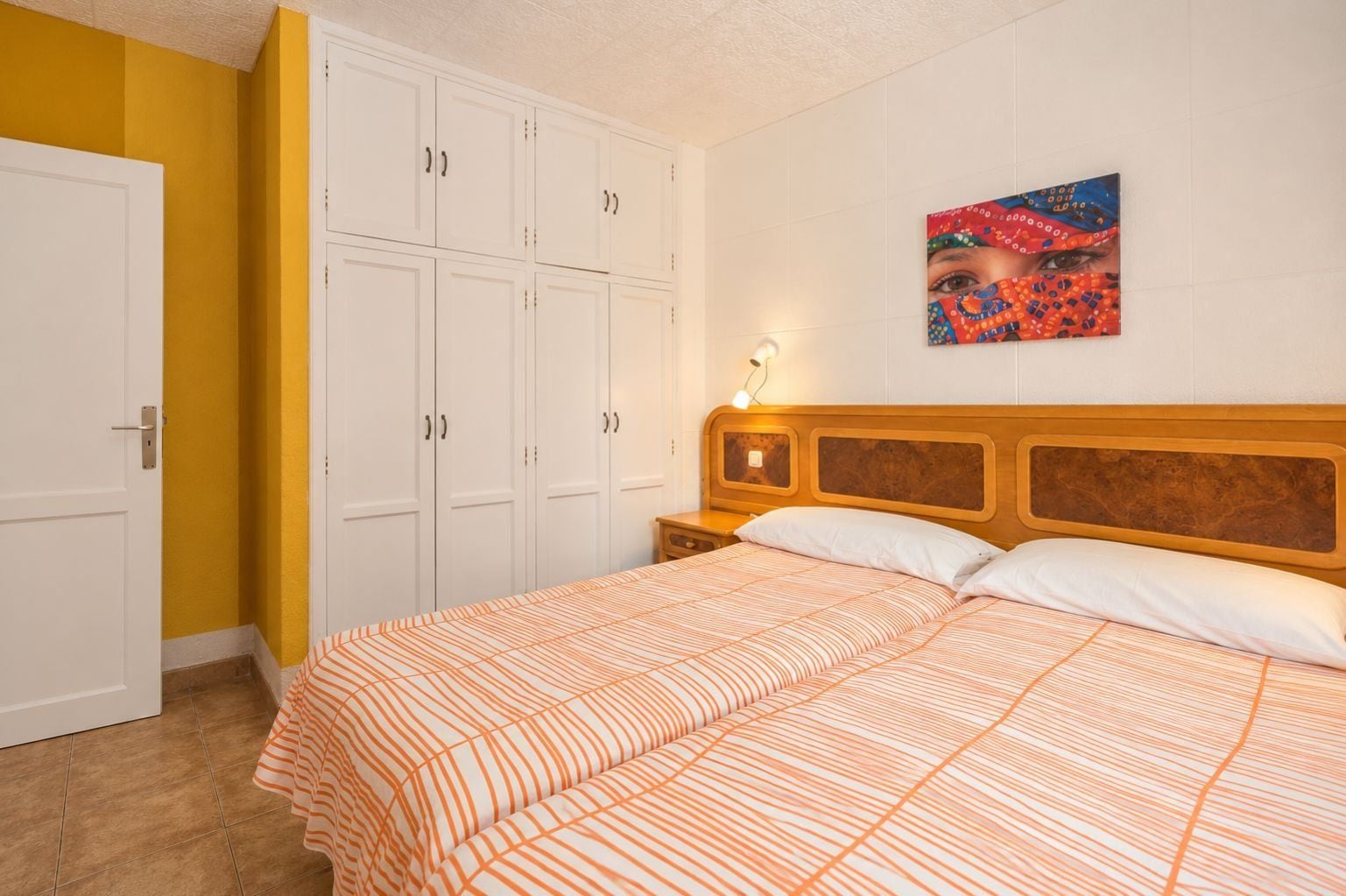 A bedroom with a bed, a nightstand, a wall-mounted lamp, and a wardrobe.