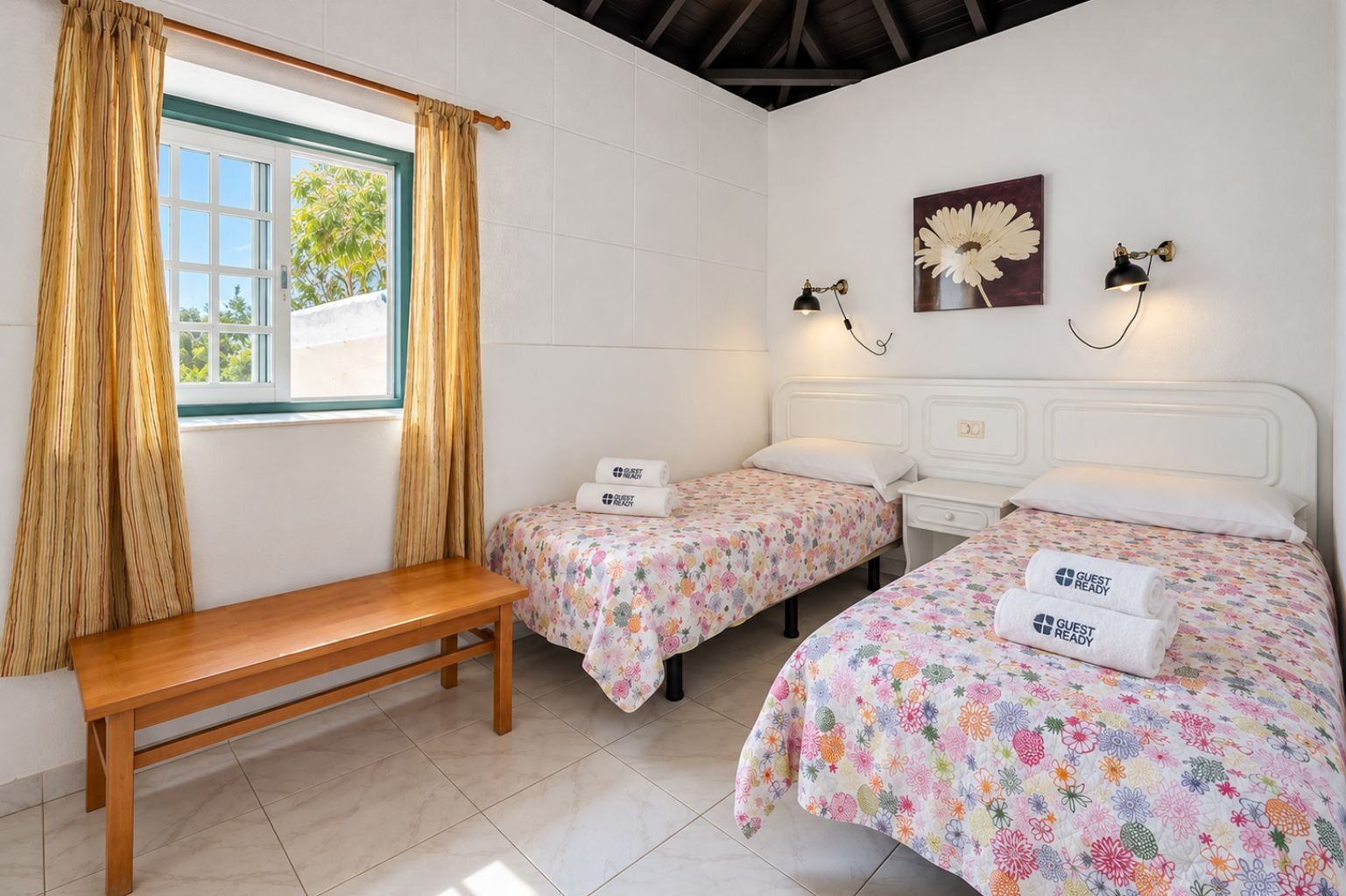 A hotel room with two beds, a bench, and a window with curtains.