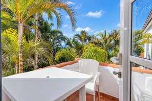 A balcony with a white table and chairs, surrounded by lush tropical vegetation.