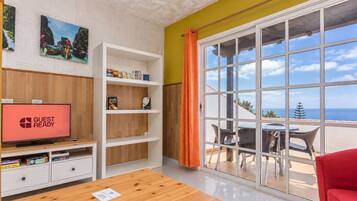 Una habitación con televisión, estanterías de madera, un sofá rojo y vistas al mar a través de amplios ventanales.