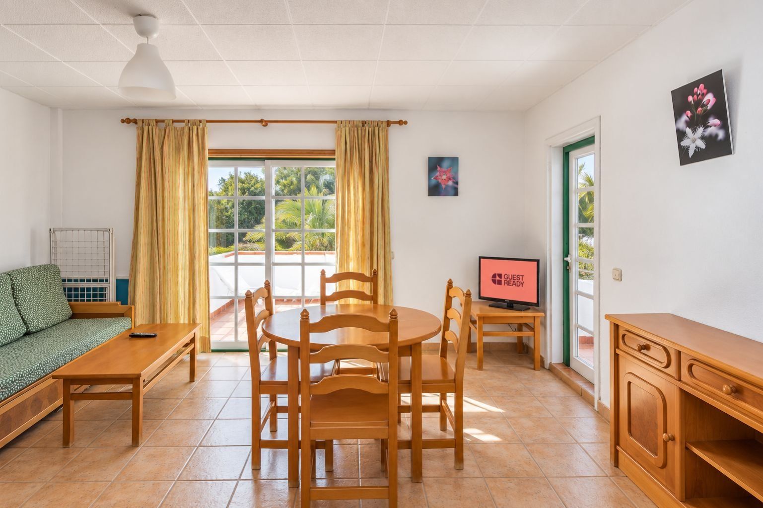 A room with a dining table, chairs, a sofa, a television, and a cabinet.