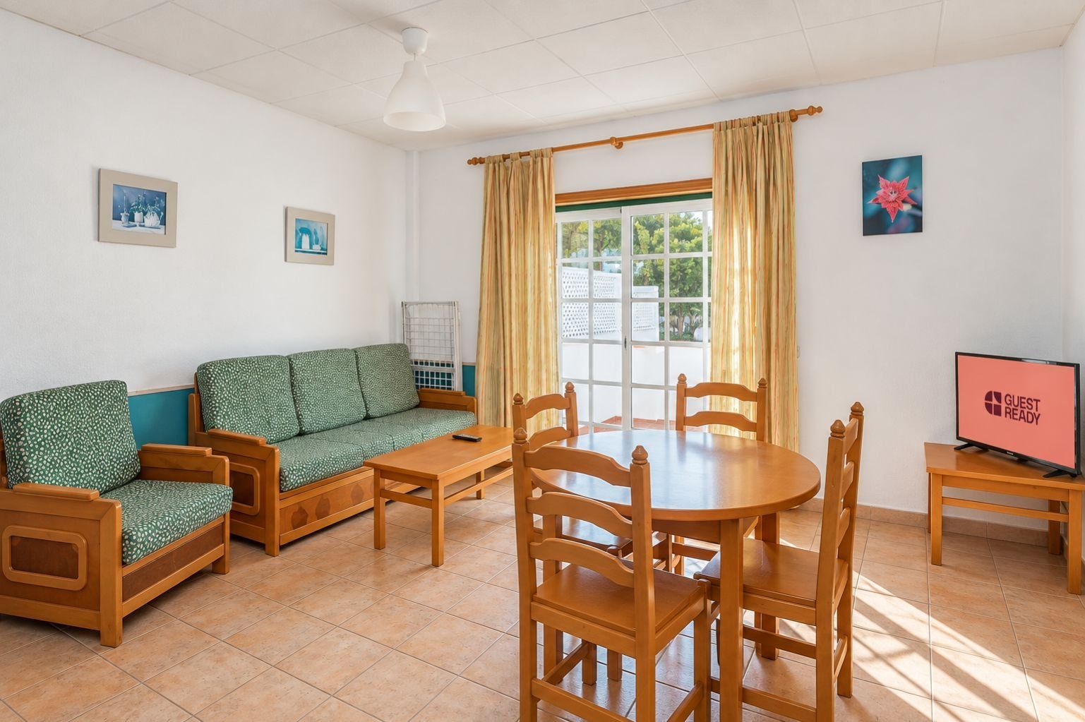 Une pièce comprenant un canapé, une table à manger avec des chaises, un téléviseur et une fenêtre avec des rideaux.