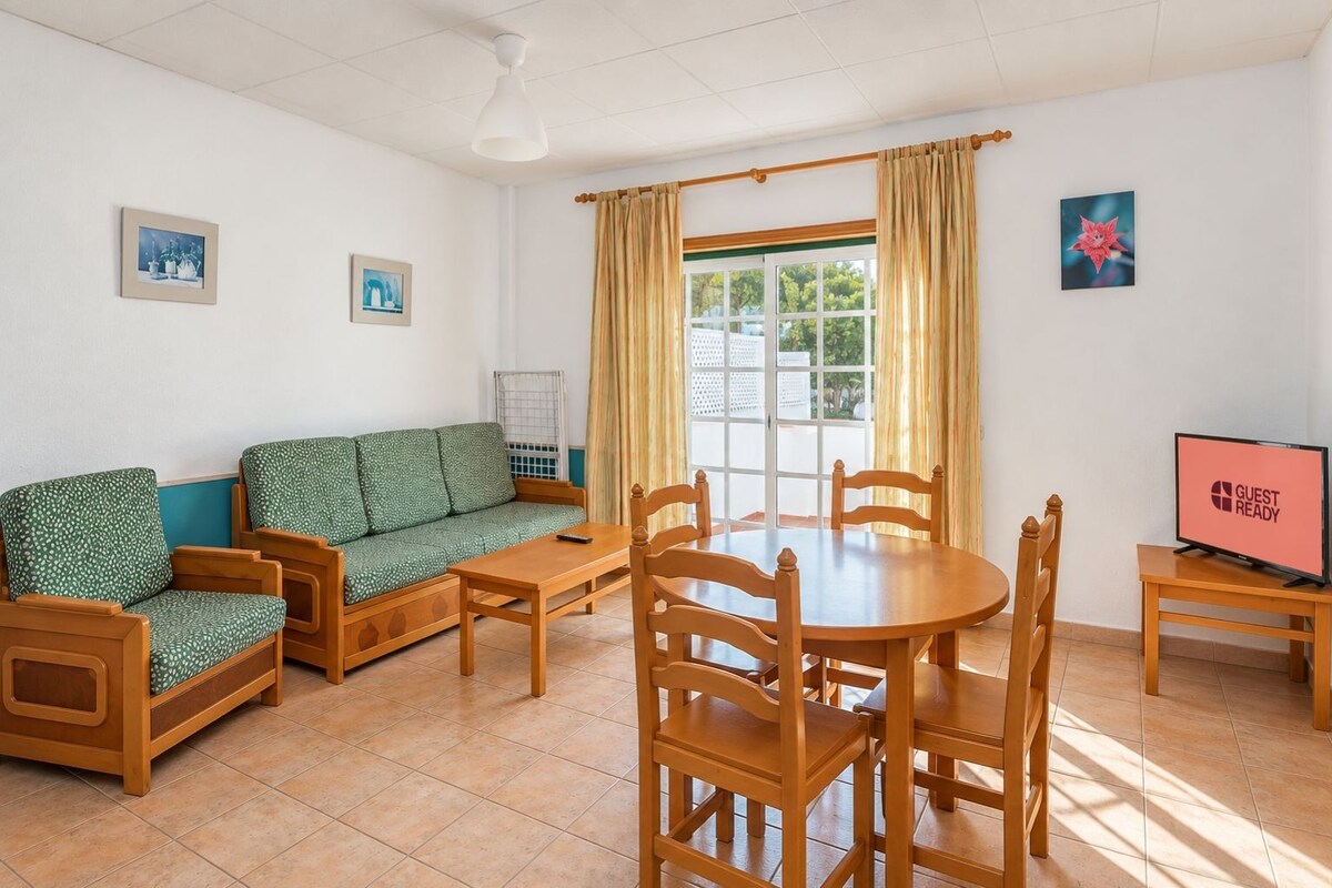 Una habitación con sofá, mesa de comedor con sillas, televisión y ventana con cortinas.