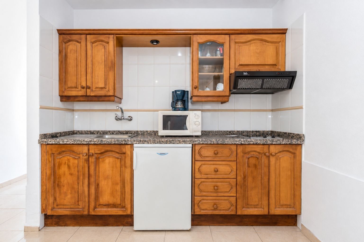 A compact kitchen with wooden cabinets, a built-in microwave, and a coffee maker.