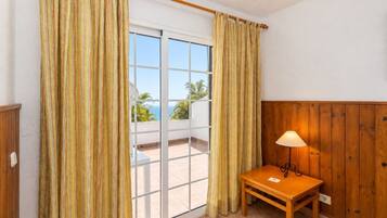 Una habitación con una mesa de madera, una lámpara y vista al océano a través de una puerta corrediza de vidrio.