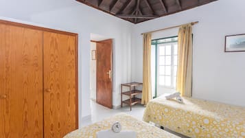 Un dormitorio con dos camas, un armario de madera, una mesita pequeña y una ventana con cortinas.