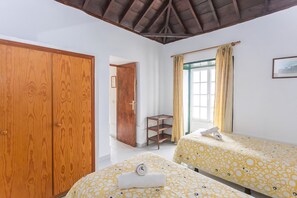 A bedroom with two beds, wooden wardrobe, a small table, and a window with curtains. - Guestready - Colon Eva (Fuencaliente de la Palma)