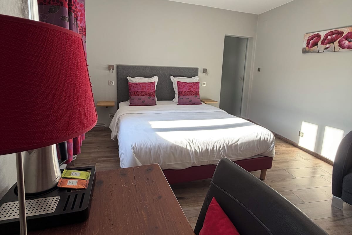 Una habitación de hotel con cama, escritorio, lámpara y un cuadro en la pared.