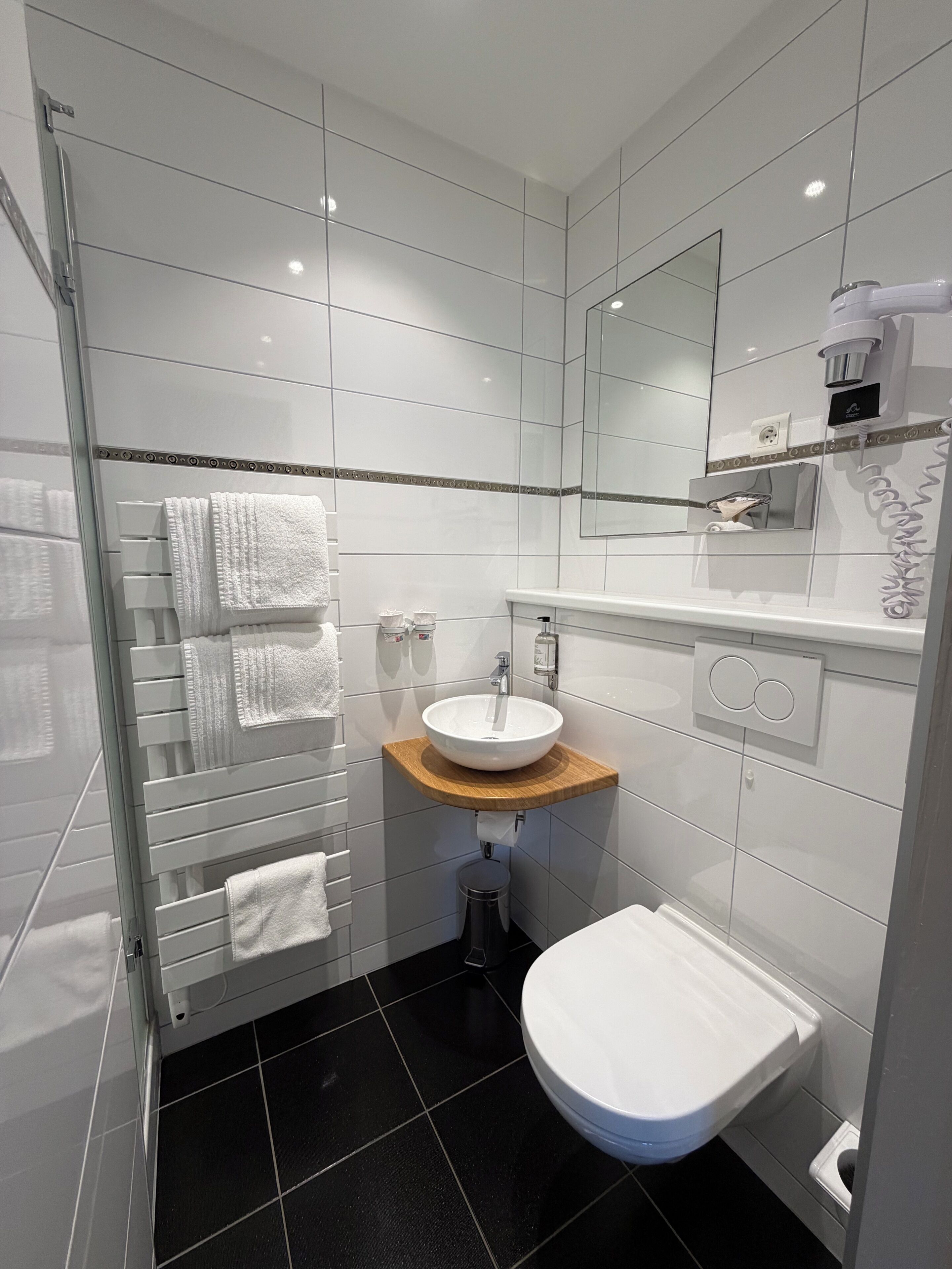 A modern bathroom with a glass shower enclosure, a white sink with a wooden countertop, a toilet, and a large mirror.