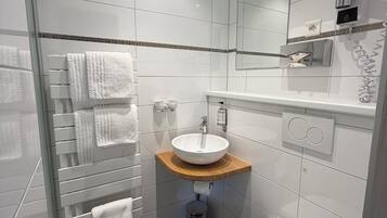 A modern bathroom with a glass shower enclosure, a white sink with a wooden countertop, a toilet, and a large mirror.