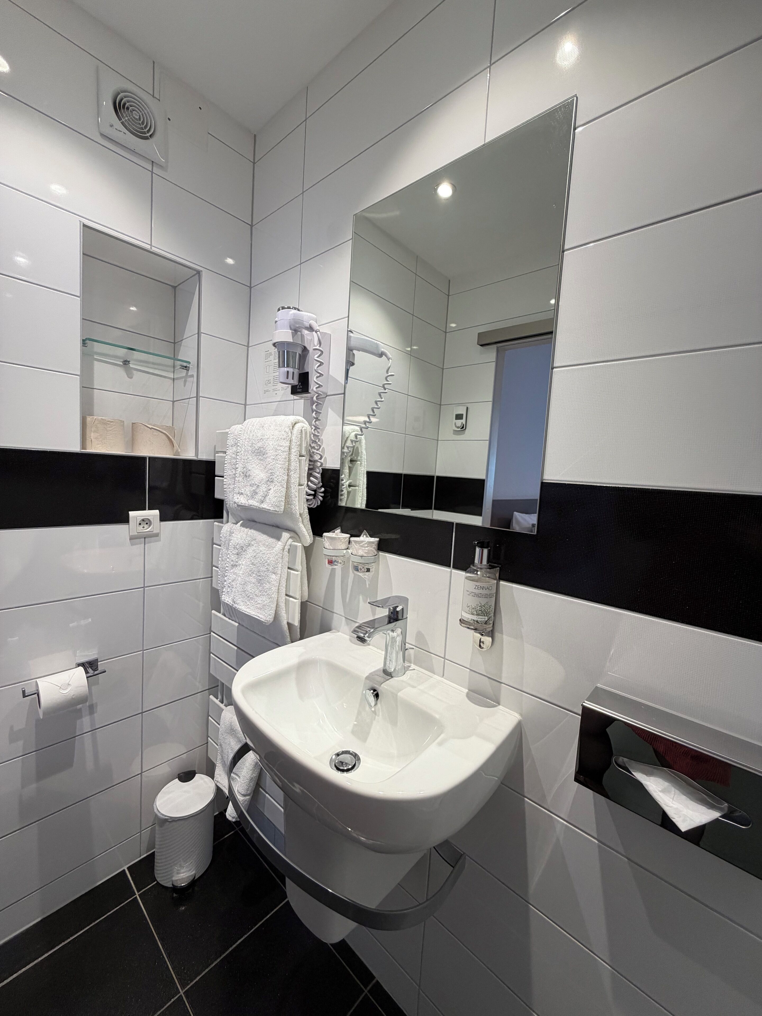 A modern bathroom with a white sink, a mirror, a towel rack, and a glass shower enclosure.