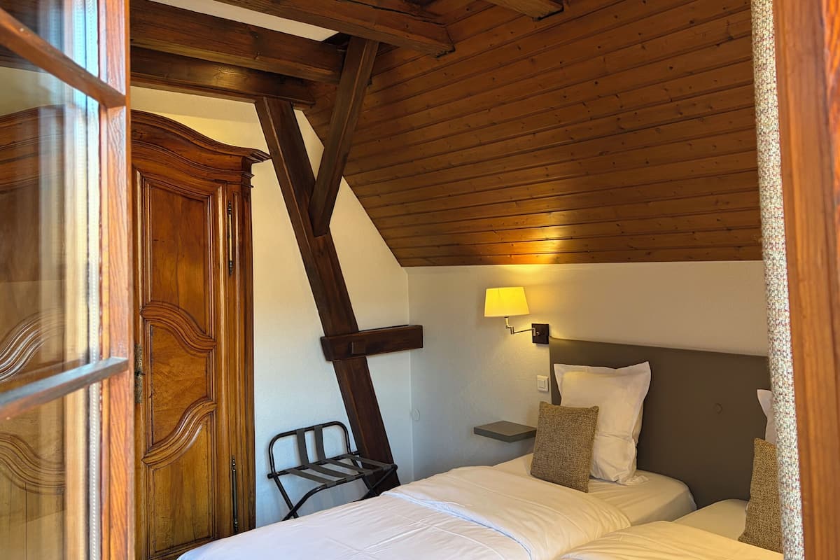 Una habitación con techo de madera, una cama con ropa blanca, una mesita de noche con lámpara y una silla.