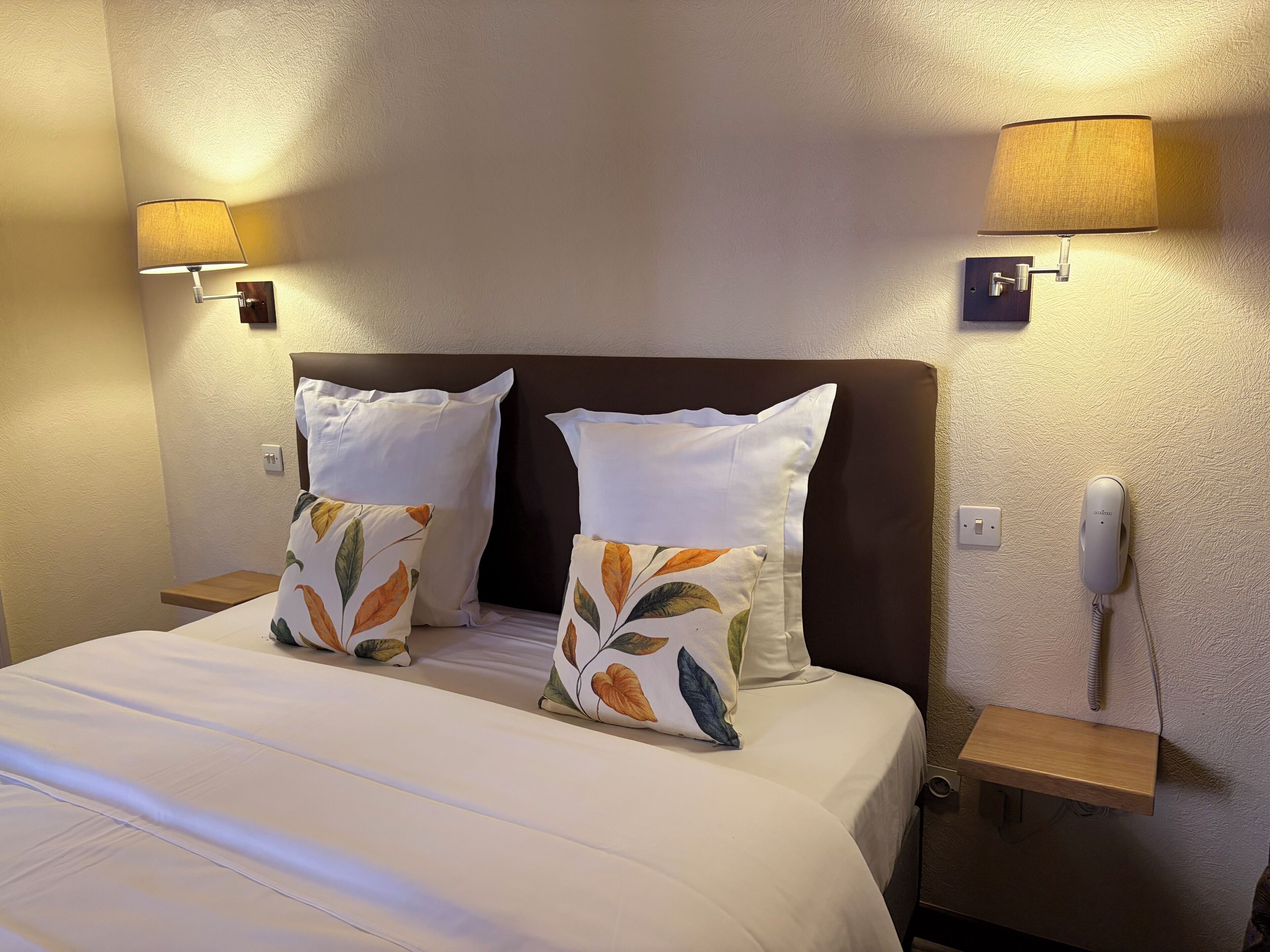 A hotel room with a bed, two pillows, bedside lamps, a phone, and a nightstand.