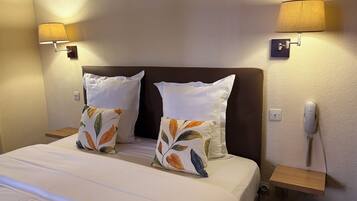 A hotel room with a bed, two pillows, bedside lamps, a phone, and a nightstand.