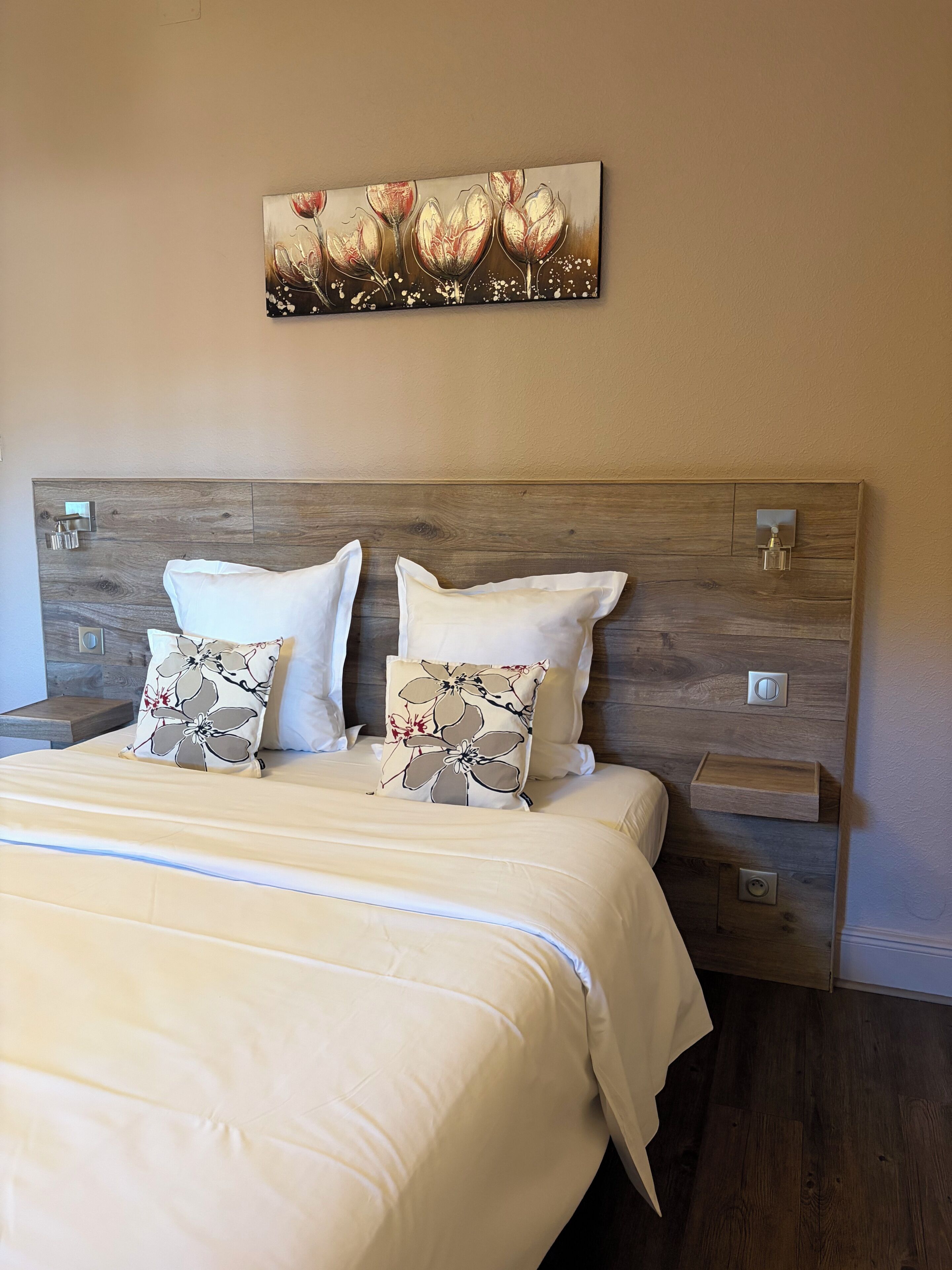 Una cama con cabecera de madera, dos almohadas blancas y una almohada con estampado floral.