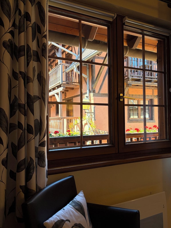 A room with a window overlooking a balcony with wooden railings and a view of a building with a wooden facade. - Hôtel-restaurant l'Ange (Niedermorschwihr)