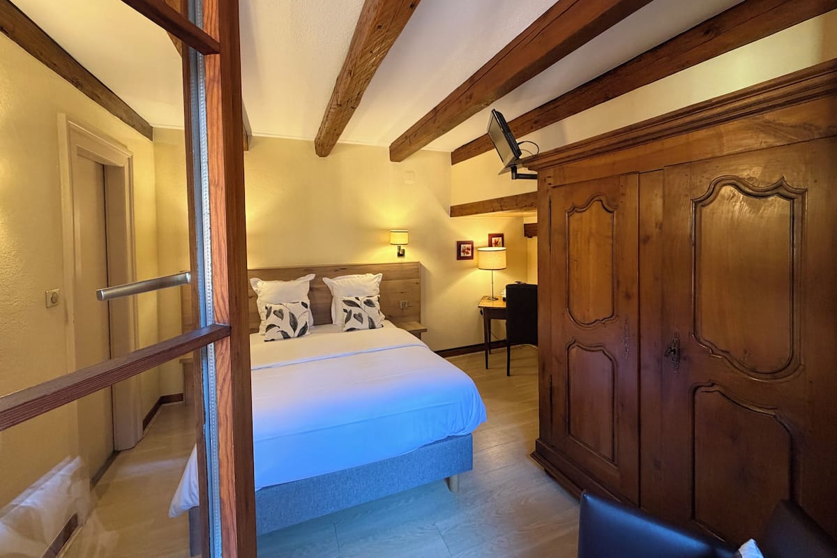 Un dormitorio con cama, armario de madera y escritorio con lámpara.