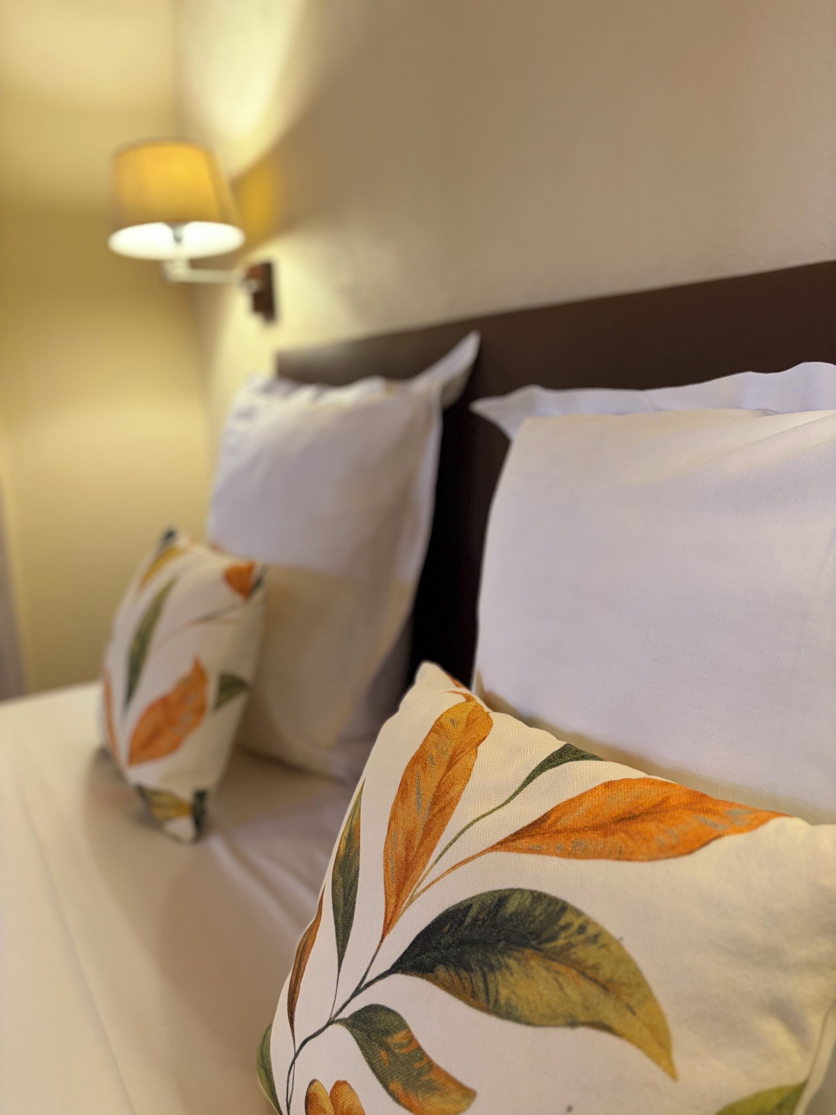 Una cama bien hecha con sábanas blancas y almohadones decorativos con diseño de hojas.