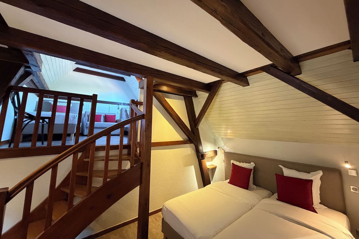 Un dormitorio con una escalera de madera, una cama con ropa de cama blanca y roja, y un techo inclinado con vigas de madera.