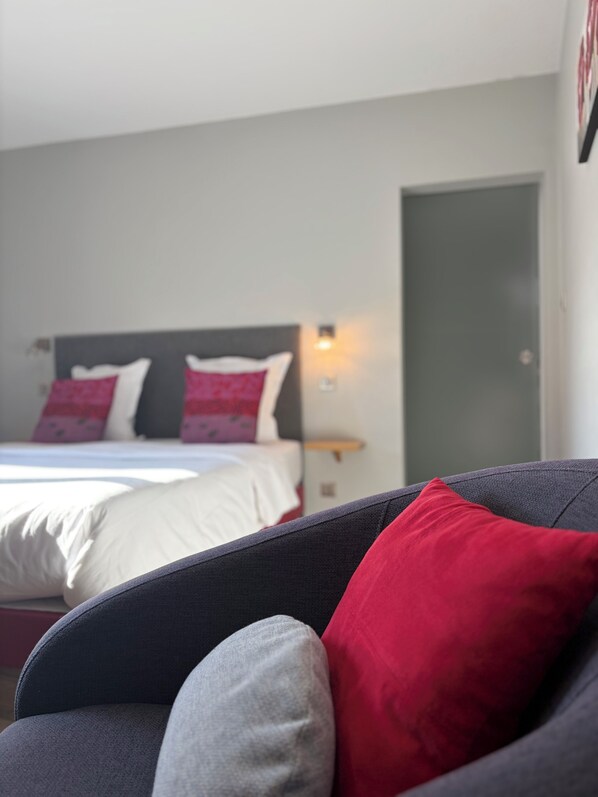 Un dormitorio con cama, almohadas, una mesita de noche y una puerta.