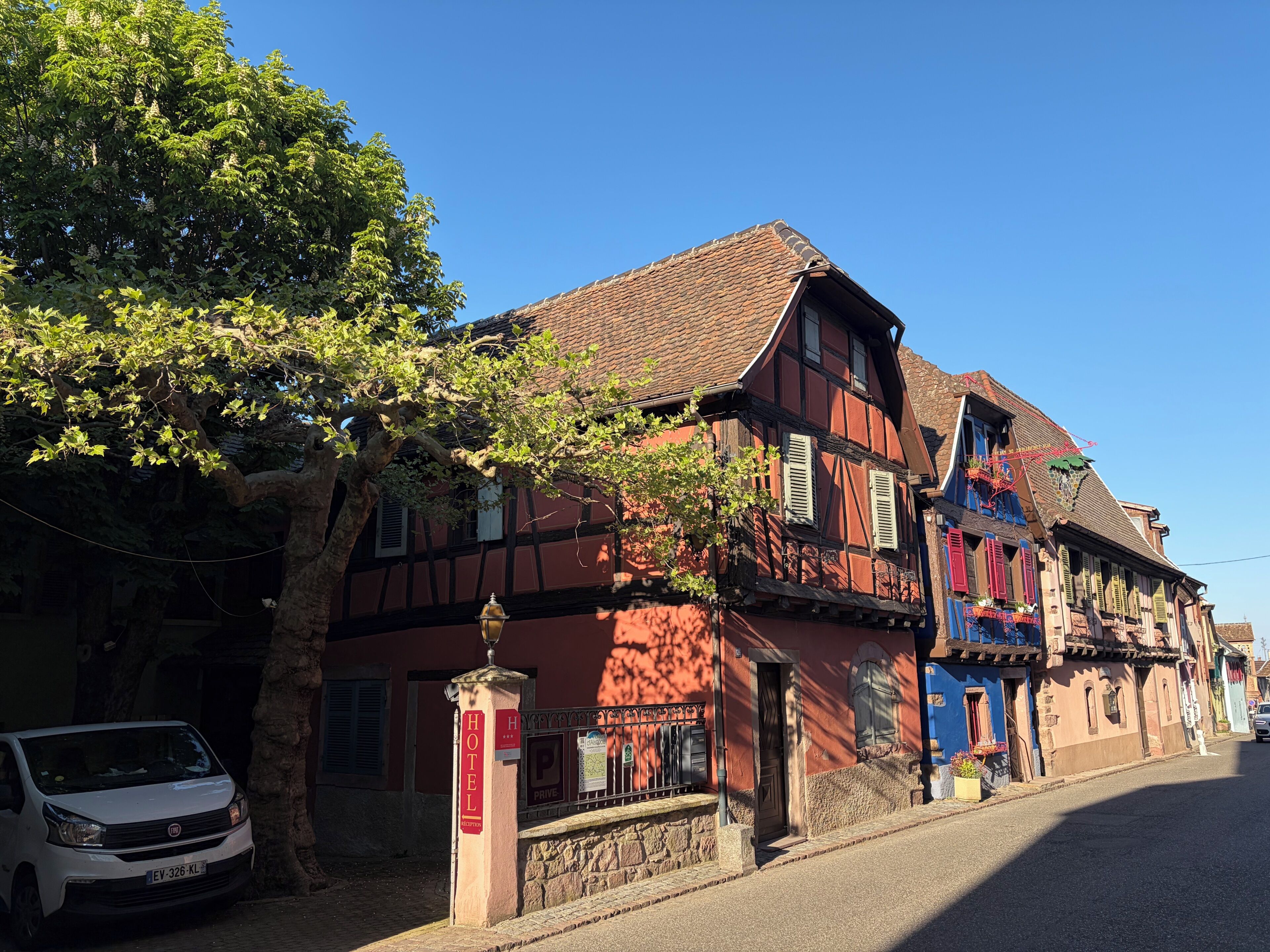 A traditional European building with a visible entrance, a parked car, and a tree in front.
