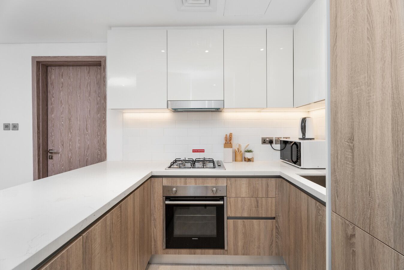 A modern kitchen with white cabinets, a built-in oven, a microwave, and a gas stove.
