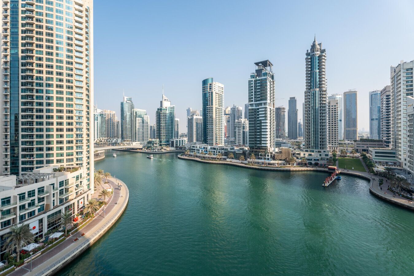 A high-rise urban area with a river, modern buildings, and a waterfront promenade.