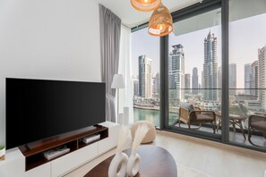A modern living room with a large TV, a white console, a decorative vase, wicker furniture, and a city view. - Gala Guests - LIV Apartments Collection (Dubai)