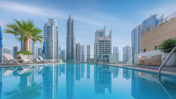 A swimming pool with lounge chairs, a palm tree, and modern high-rise buildings in the background. - Gala Guests - LIV Apartments Collection (Dubai)