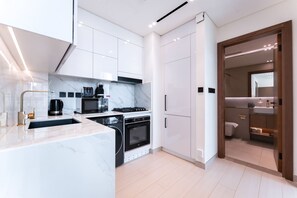 Una cocina moderna con armarios blancos, horno empotrado y cafetera.