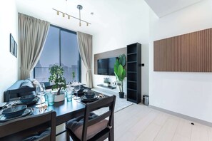 Un comedor moderno con una mesa preparada para cuatro personas, un ventanal con cortinas, una planta en maceta y un televisor montado en la pared.