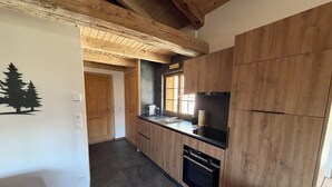 A modern kitchen with wooden cabinets, a black countertop, and a built-in oven. - Le mazot - large studio with separate shower room (Lens)