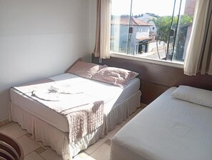 Un dormitori amb un llit, una finestra amb cortines i vista a edificis.