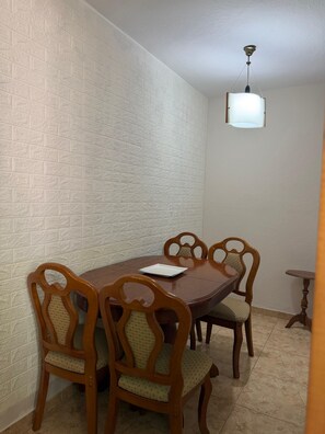 Ein Essbereich mit Holztisch und -stühlen, einer weißen Wand mit Struktur und einer hängenden Leuchte.