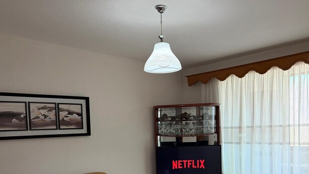 A living room with a sofa, a coffee table, a television, and a ceiling light.