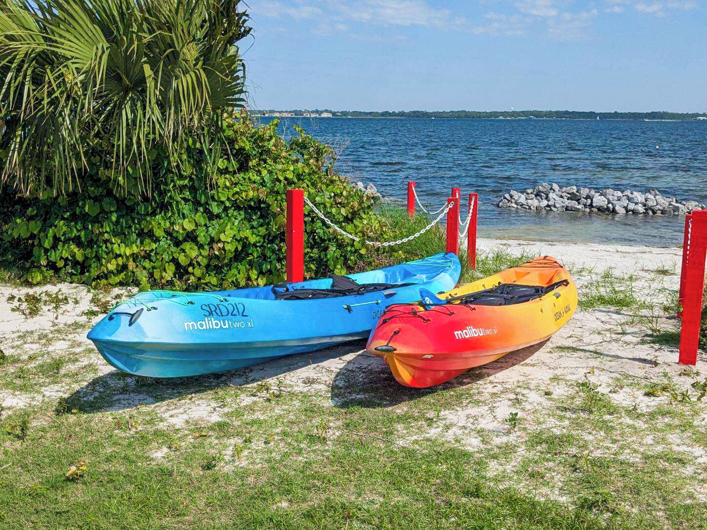 Tres kayaks sobre una playa arenosa con una masa de agua y una costa lejana al fondo.
