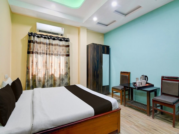 A hotel room with a bed, a desk with a chair, a wardrobe, and an air conditioning unit.