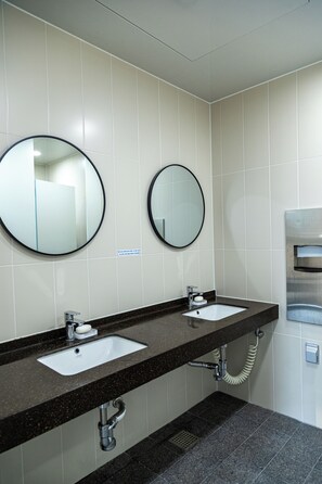 A bathroom with two sinks, two round mirrors, and a hand dryer. - Lazy Cube (Seoul)