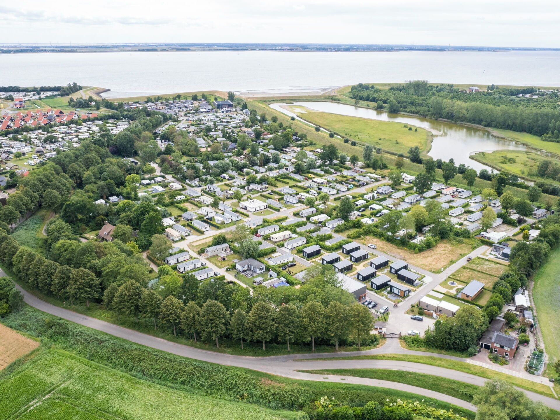 An aerial view of a residential area with houses arranged in a grid pattern, surrounded by greenery and a body of water.